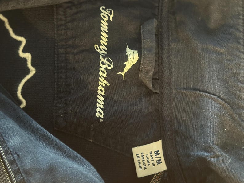 May include: Close-up of a navy blue garment tag with the Tommy Bahama logo and text. The tag also includes size information and the text "Made in China / Fabriqu&eacute; en Chine".