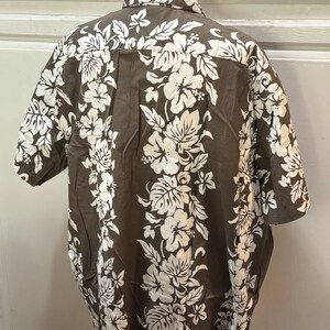 May include: A brown short-sleeved shirt with a white floral pattern. The shirt has a button-up collar and a button-up front.