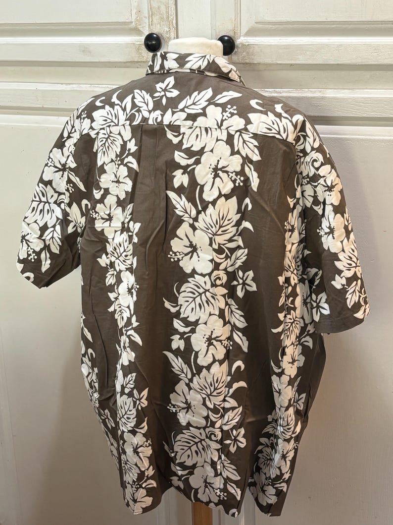 May include: A brown short-sleeved shirt with a white floral pattern. The shirt has a button-up collar and a button-up front.