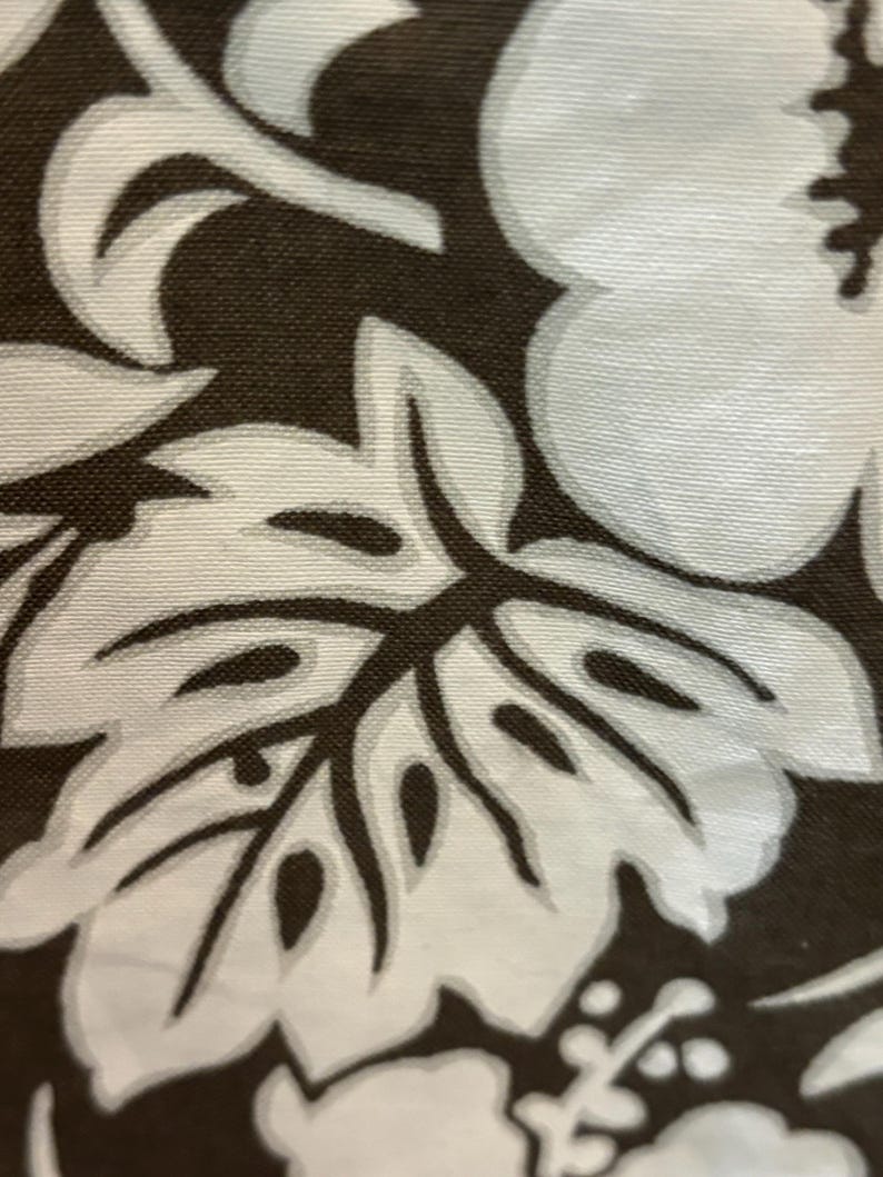 May include: A close-up of a brown fabric with a white floral pattern. The pattern features large hibiscus flowers and leaves.