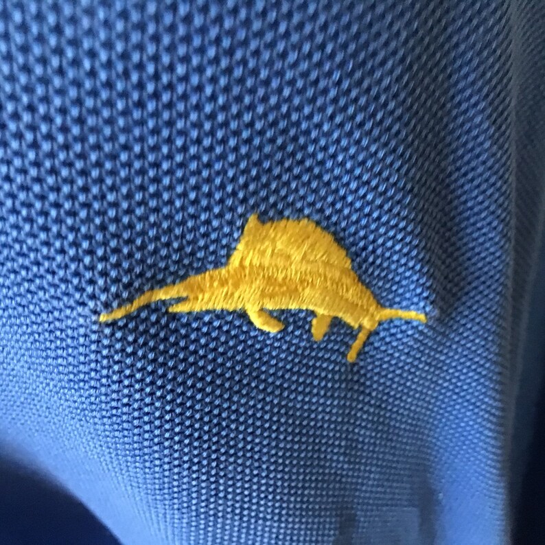 May include: A yellow embroidered marlin fish logo on a blue polo shirt.