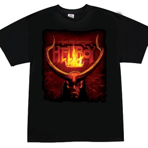 May include: Black t-shirt featuring a graphic of Hellboy with the text "HELLBOY" in orange and yellow flames. The image includes a depiction of Hellboy's face and horns, with the phrase "DEMONS HAVE DEMONS TOO" above the logo.