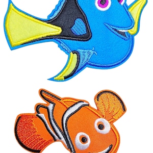 Könnte beinhalten: Zwei bestickte Stoffaufnäher mit Zeichentrickfisch-Motiven. Der obere Aufnäher zeigt einen blauen und schwarzen Fisch mit gelben Flossen und einem pinken Auge. Der untere Aufnäher ist ein orange-weiß gestreifter Fisch mit schwarzen Umrandungen.