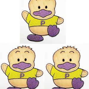 May include: Embroidered duck patch with a yellow shirt, purple beak, feet, and the letter "P". The duck has a tan body and is waving. The patch is likely for clothing or accessories.