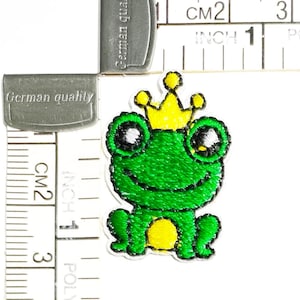 May include: Green frog wearing a yellow crown, embroidered iron-on patch, approximately 1 inch wide.