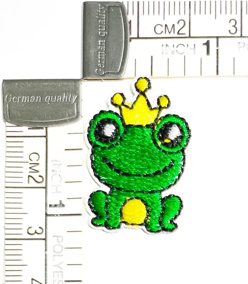 May include: Green frog wearing a yellow crown, embroidered iron-on patch, approximately 1 inch wide.