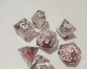Puede incluir: Un juego de siete dados poliédricos hechos de resina transparente, cada uno con motivos de naipes en miniatura. Los dados presentan números blancos e incluyen varias formas como d20, d12, d10, d8, d6 y d4, mostrando símbolos de cartas.