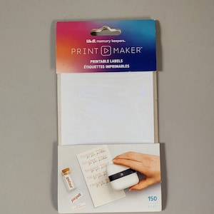 May include: A package of 150 printable labels for the We R Memory Keepers Print Maker. The package shows a white sheet of labels and a hand holding the Print Maker, which is a small white device with a black logo. The labels are printed with the text "Thank You for your purchase".