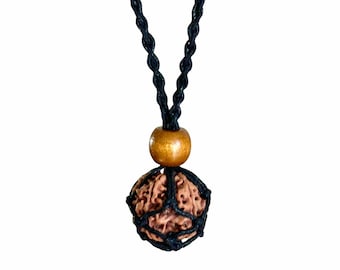 May include: A necklace featuring a brown, textured seed pendant encased in a black net. The pendant is suspended from a black cord, with a wooden bead accent. The background is plain white.