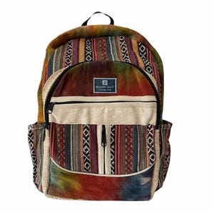 May include: A multi-colored woven backpack with a large front pocket and a smaller pocket on each side. The backpack has a tie-dye pattern on the top and bottom and a cream-colored fabric panel in the middle. The brand name "SOLAR FAIT" is printed on the cream-colored panel.