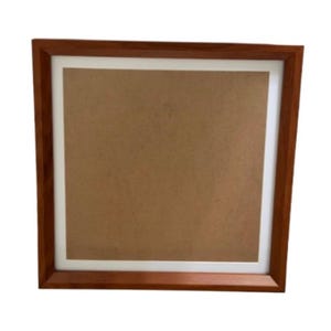 May include: A square picture frame featuring a medium-toned brown wooden border and a white matting surrounding a plain, light brown cardboard backing. The frame has a clean, simple design with mitered corners and a smooth, polished finish.