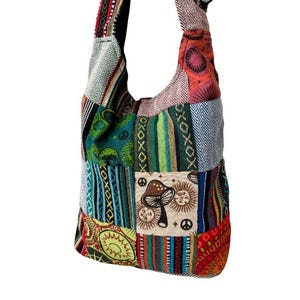 May include: A colourful patchwork shoulder bag with various fabric patterns. The bag features geometric, floral, and abstract designs in green, blue, red, and orange. A central patch displays a mushroom and sun graphic.