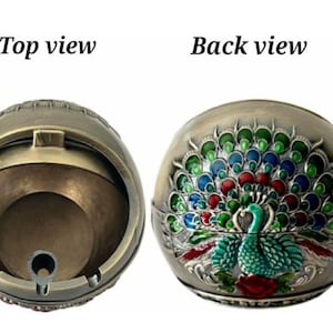 May include: A decorative ashtray with a peacock design. The front view shows a detailed peacock with a fanned tail in shades of green, blue, and red. The top view shows the inside of the ashtray. The text "Top view" and "Back view" are visible.