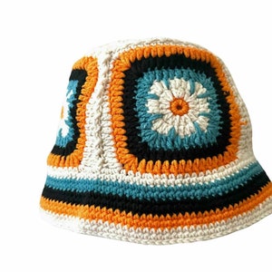 May include: A white crocheted bucket hat with orange, black, and blue stripes and a floral design.