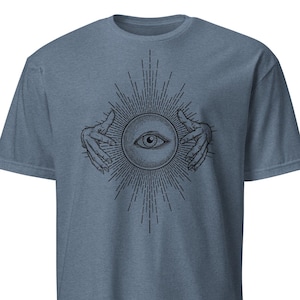 Op de afbeelding: Blauw t-shirt met zwarte afbeelding. De afbeelding toont een oog in een cirkel, omringd door stralende lijnen en handen. Het ontwerp is gecentreerd op de voorkant. Het shirt heeft korte mouwen en een ronde hals.