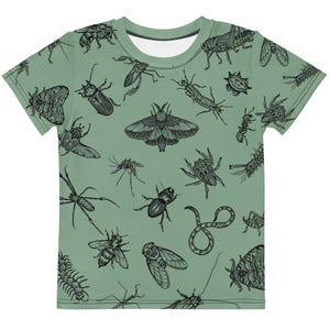 May include: Sage green t-shirt featuring a repeating pattern of various black insect illustrations, including moths, beetles, spiders, and ants. The shirt has a crew neck and short sleeves, suitable for casual wear.