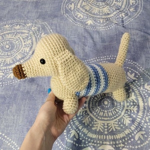 May include: A crocheted dachshund dog toy with a cream-colored body and blue and white striped accents.