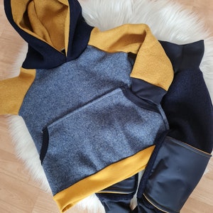 Könnte beinhalten: Ein blaues und gelbes Kapuzenpullover und eine passende Hose. Der Pullover hat eine gelbe Kapuze und gelbe Akzente an den Ärmeln und am Saum. Die Hose ist blau mit gelben Akzenten an den Beinen.