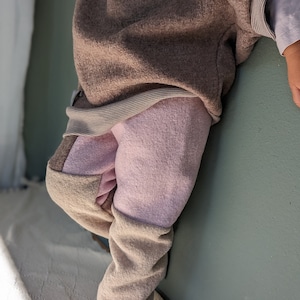 Può includere: Un paio di pantaloni in pile rosa e marrone con un bordo marrone a contrasto. I pantaloni sono realizzati in un materiale morbido e soffice e hanno una vestibilità rilassata.