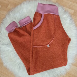 May include: Orange and pink sweatpants with a large pocket on the left leg. The pocket has a pink trim and a small label with the text "VIS" on it.
