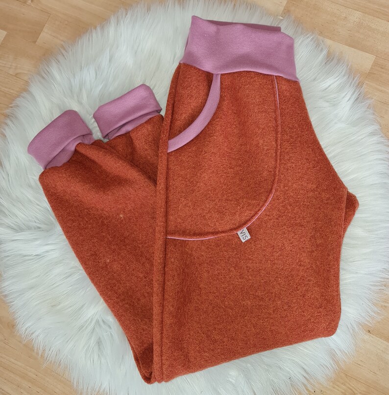 May include: Orange and pink sweatpants with a large pocket on the left leg. The pocket has a pink trim and a small label with the text "VIS" on it.