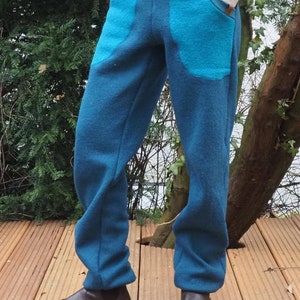 May include: Blue fleece pants with large turquoise pockets. The pants are worn by a person standing on a wooden deck.