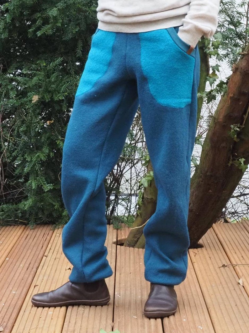 May include: Blue fleece pants with large turquoise pockets. The pants are worn by a person standing on a wooden deck.