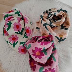 Può includere: Tre bavaglini per bambini con motivi floreali. I bavaglini presentano una varietà di colori, tra cui rosa, verde e crema. Sono realizzati in un tessuto morbido e strutturato, disposti su una superficie bianca e soffice.