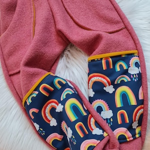 Op de afbeelding: Roze fleece broek met regenboog- en wolkendruk stofpanelen op de benen. De panelen hebben een gele bies.