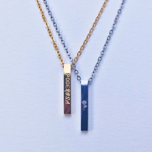 May include: Two necklaces with bar pendants. One pendant is gold-colored with the word "PODEROSA" in gold lettering. The other pendant is silver-colored with a small rose design. Both necklaces have delicate chain links.