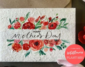 Peut inclure: Une carte blanche avec des fleurs de couleur rouge et rose et des feuilles vertes peintes à l'aquarelle. La carte dit "Joyeuse fête des mères" en écriture noire. La carte est faite de papier plantable et dit "Je me transforme en fleurs sauvages PLANTEZ-MOI !" dans un cercle rouge.
