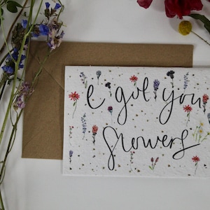 May include: A greetings card with the handwritten text "I got you flowers" and small floral illustrations. A brown envelope and dried flowers in purple, red, and yellow are also present.
