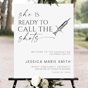 May include: A white graduation sign with the text "she IS READY TO CALL THE shots" and a syringe illustration. The sign welcomes guests to Jessica Marie Smith's graduation celebration from North Singularity University.