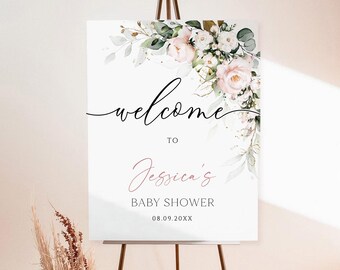 May include: A white welcome sign on a dark brown easel, decorated with watercolor flowers and greenery. The sign reads "welcome to Jessica's Baby Shower" with the date 08.09.XX. A vase of dried flowers and palm leaves sits to the left.