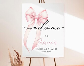 May include: A white sign on a dark metal easel with a pink bow and the word "welcome" in script. The sign reads "Welcome to Jessica's Baby Shower 08.09.20XX". A vase of dried flowers and a decorative fan sits on the floor.