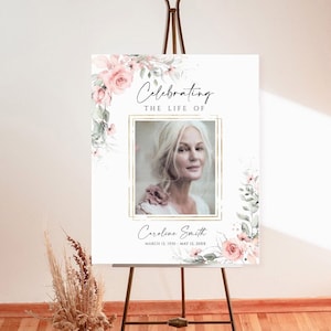 May include: A white memorial sign with a floral border and a photo of a woman. The sign reads "Celebrating the Life of Caroline Smith, March 12, 1959 - May 12, 20XX".