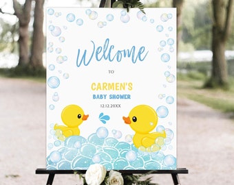 May include: Welcome to Carmen's Baby Shower sign with a blue and yellow color scheme. The sign features two yellow rubber duckies in a blue bathtub with white bubbles. The text on the sign reads "Welcome to Carmen's Baby Shower 12.12.20XX".