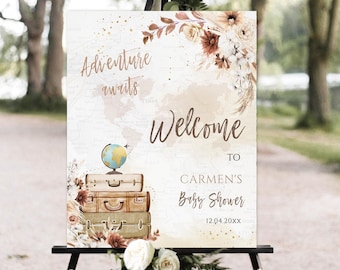Puede incluir: Un cartel de bienvenida para un baby shower con temática de viaje. El cartel presenta un mapa del mundo, maletas, un globo terráqueo y detalles florales en tonos marrones, beige y blanco. El texto dice "La aventura te espera, Bienvenida a la fiesta de bienvenida de Carmen 12.04.20XX".