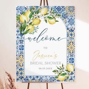 May include: A welcome sign for Jessica's bridal shower, featuring a lemon and floral design. The sign is displayed on a brown metal easel. The sign has a blue and yellow tile border and the text "welcome to Jessica's bridal shower".