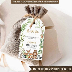 May include: A white thank you tag with a gold border and green foliage design. The text reads "Thank You for showering us with love Carmen's Baby Shower July 24th, 2024". There are woodland animals in the design, including a bear, fox, deer, raccoon, and squirrel.