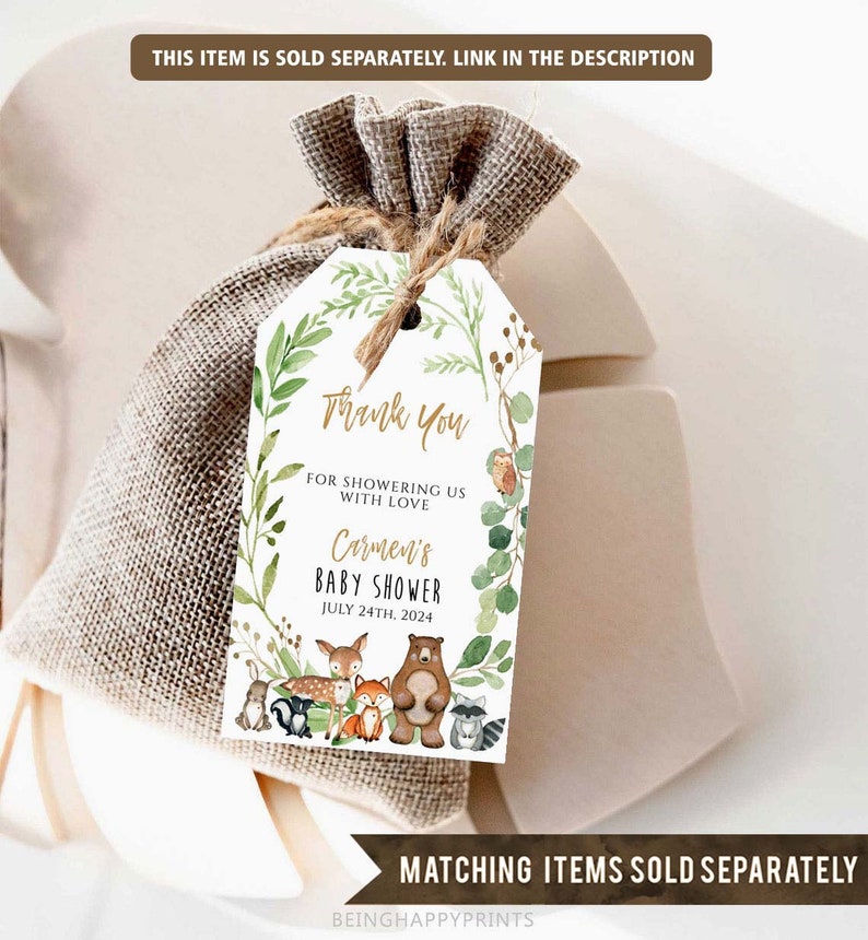 May include: A white thank you tag with a gold border and green foliage design. The text reads "Thank You for showering us with love Carmen's Baby Shower July 24th, 2024". There are woodland animals in the design, including a bear, fox, deer, raccoon, and squirrel.