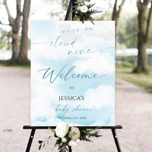 May include: A blue and white watercolor baby shower welcome sign with the text "We're on cloud nine. Welcome to Jessica's baby shower. October 21st, 20XX".