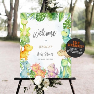 May include: Welcome to Jessica's Baby Shower sign with a jungle theme. The sign features a watercolor illustration of dinosaurs and tropical leaves. The text on the sign reads "Welcome to Jessica's Baby Shower, October 21st, 20XX".