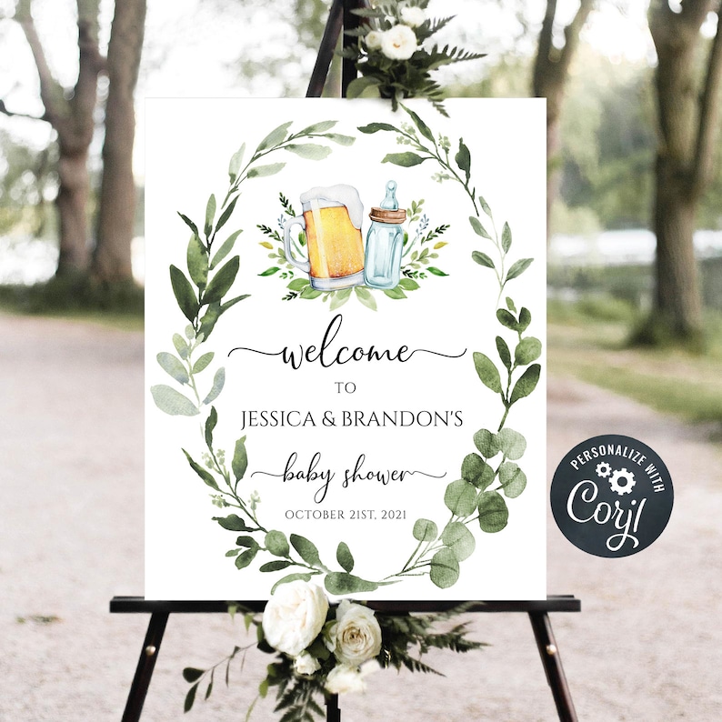 May include: A welcome sign for a baby shower with a green leafy wreath design. The wreath has a beer mug and a baby bottle inside. The text reads "Welcome to Jessica & Brandon's baby shower October 21st, 2021".