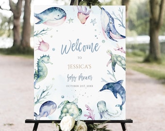 May include: Welcome to Jessica's baby shower sign with a watercolor design featuring sea creatures like whales, seahorses, turtles, and dolphins. The sign is on a wooden easel and has the date October 21st, 20XX.