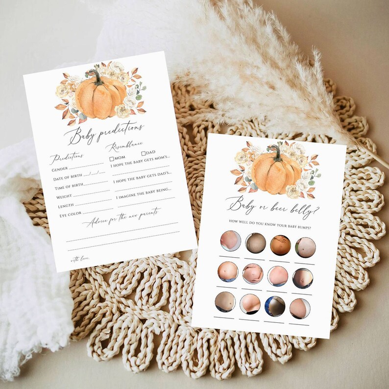 May include: Two white paper game cards featuring watercolor pumpkin and floral illustrations. One card is titled Baby predictions with fields for birth details. The other card is titled Baby or beer belly? and displays twelve circular photos of bellies.