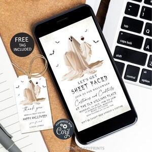 Może przedstawiać: Smartfon wyświetla zaproszenie na imprezę Halloween z ilustracją ducha trzymającego kieliszek wina. Dołączona jest pasująca etykieta prezentowa z tym samym wzorem ducha i tekstem "Thank you, Happy Halloween". Tekst zaproszenia brzmi "Let's Get Sheet Faced."