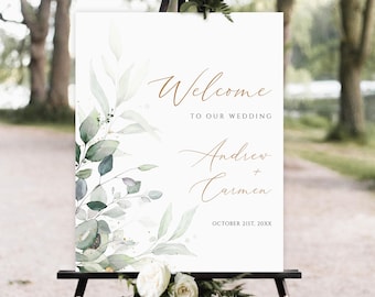 May include: A white wedding welcome sign with a watercolor design of green leaves and gold accents. The text reads "Welcome to our wedding Andrew + Carmen October 21st, 20XX".