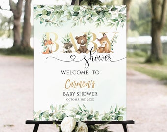 Op de afbeelding: Een wit welkomstschild voor een babyshower met gouden letters waarop 'Baby Shower' staat. Het bord is versierd met groene eucalyptusbladeren en heeft een schattige illustratie van bosdieren, waaronder een vos, een wasbeer, een beer en een hert. De tekst 'Welkom bij Carmen's Baby Shower October 21st, 20XX' is ook opgenomen.