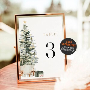 May include: A framed table number 3 with a watercolor Christmas tree illustration. The tree is decorated with ornaments and a star. The words "TABLE" and the number "3" are displayed in elegant fonts. A sticker says "SOLD SEPARATELY".